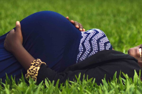 Pregnant woman laying on grass smiling holding her bump