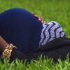 Pregnant woman laying on grass smiling holding her bump